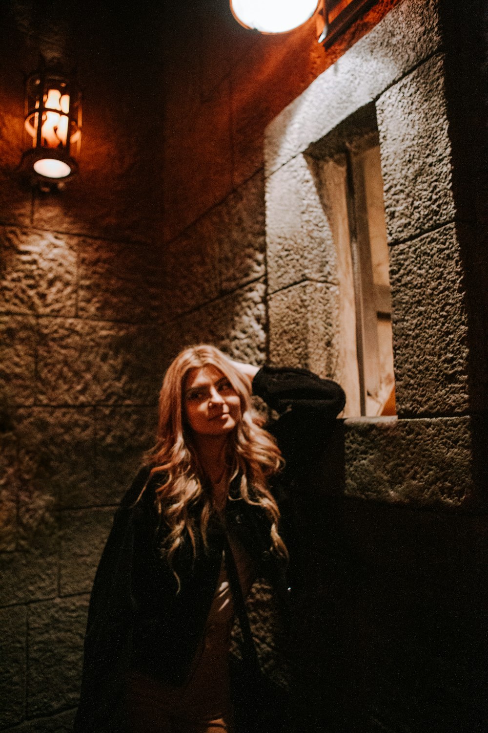 woman in black leather jacket standing beside brown brick wall