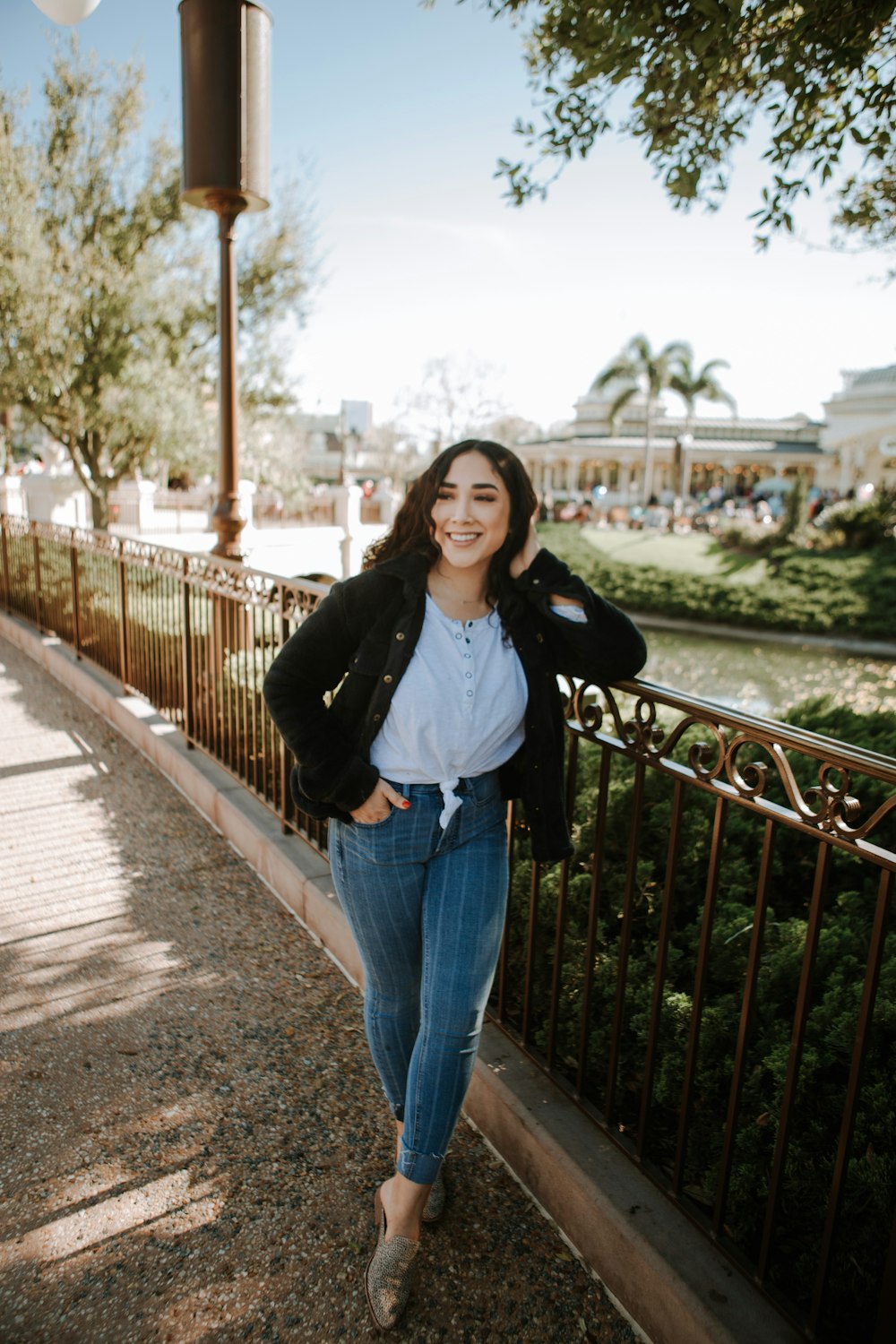 woman in black jacket and blue denim jeans standing on bridge during daytime