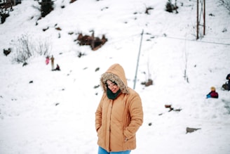woman in brown jacket and brown knit cap standing on snow covered ground during daytime