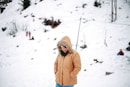 woman in brown jacket and brown knit cap standing on snow covered ground during daytime