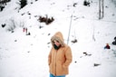 woman in brown jacket and brown knit cap standing on snow covered ground during daytime