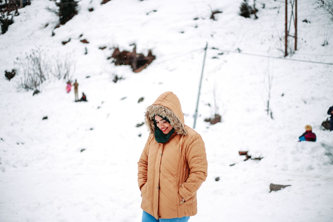 woman in brown jacket and brown knit cap standing on snow covered ground during daytime