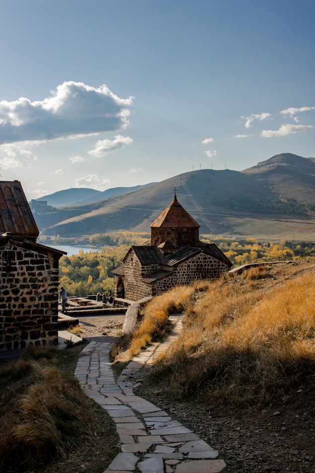 brown concrete house on green grass field near mountain under white clouds during daytime