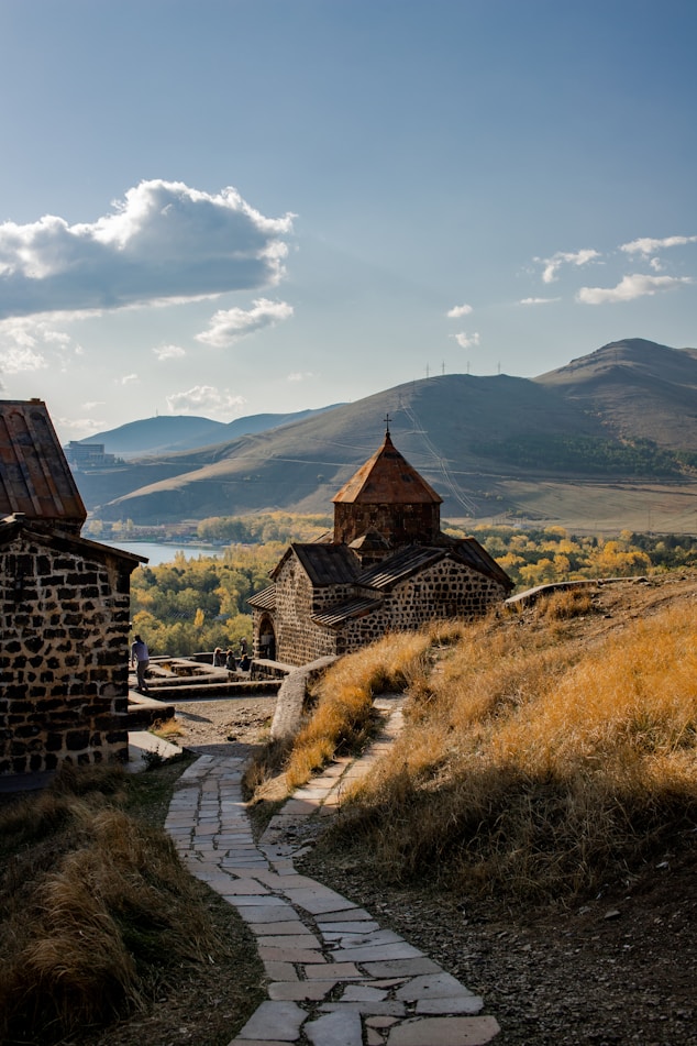 brown concrete house on green grass field near mountain under white clouds during daytime