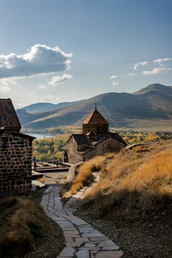 brown concrete house on green grass field near mountain under white clouds during daytime