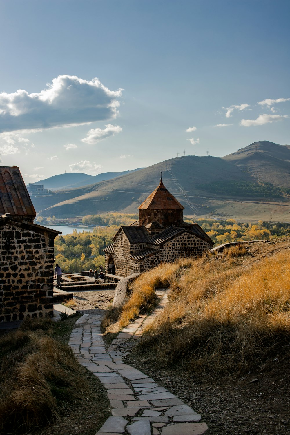 brown concrete house on green grass field near mountain under white clouds during daytime