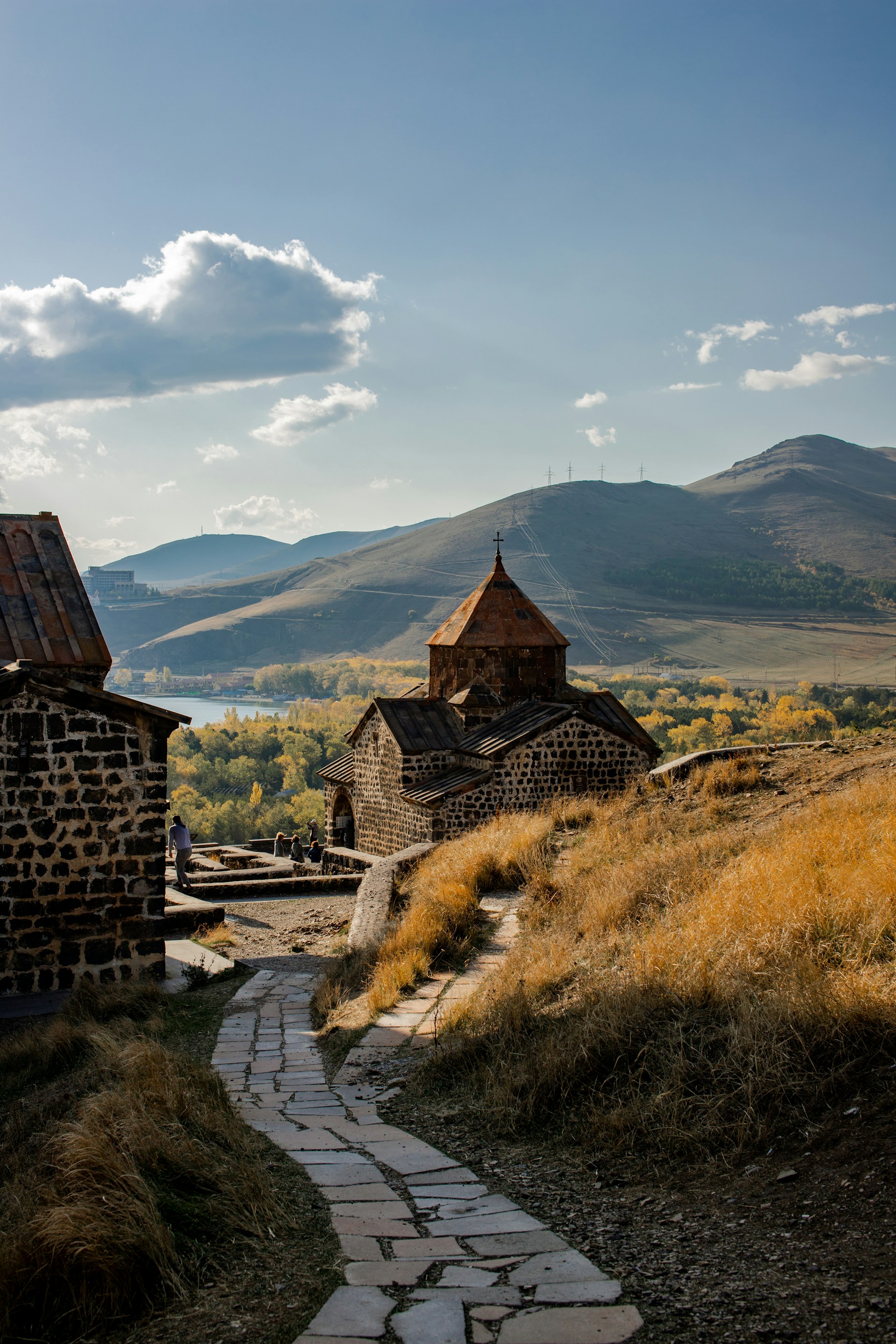 brown concrete house on green grass field near mountain under white clouds during daytime