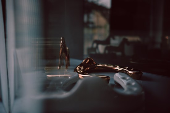 A dimly lit scene featuring reflective metallic and ceramic objects on a surface, with abstract shadows in the background creating a moody and introspective atmosphere.