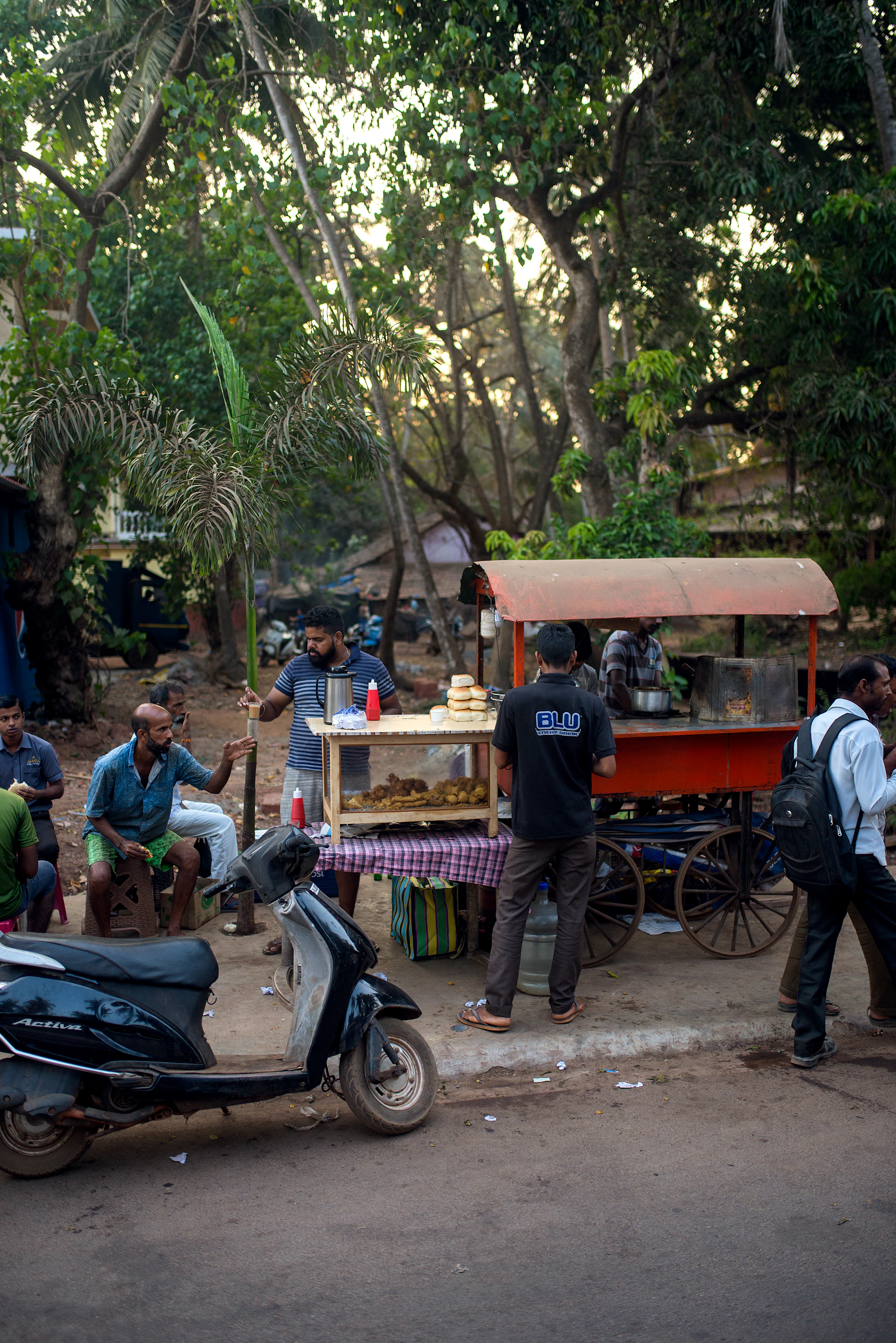 A vibrant street cart painted in orange and black, with Uncle Larry Momos signage, bustling with happy customers enjoying fried momos and spring rolls.