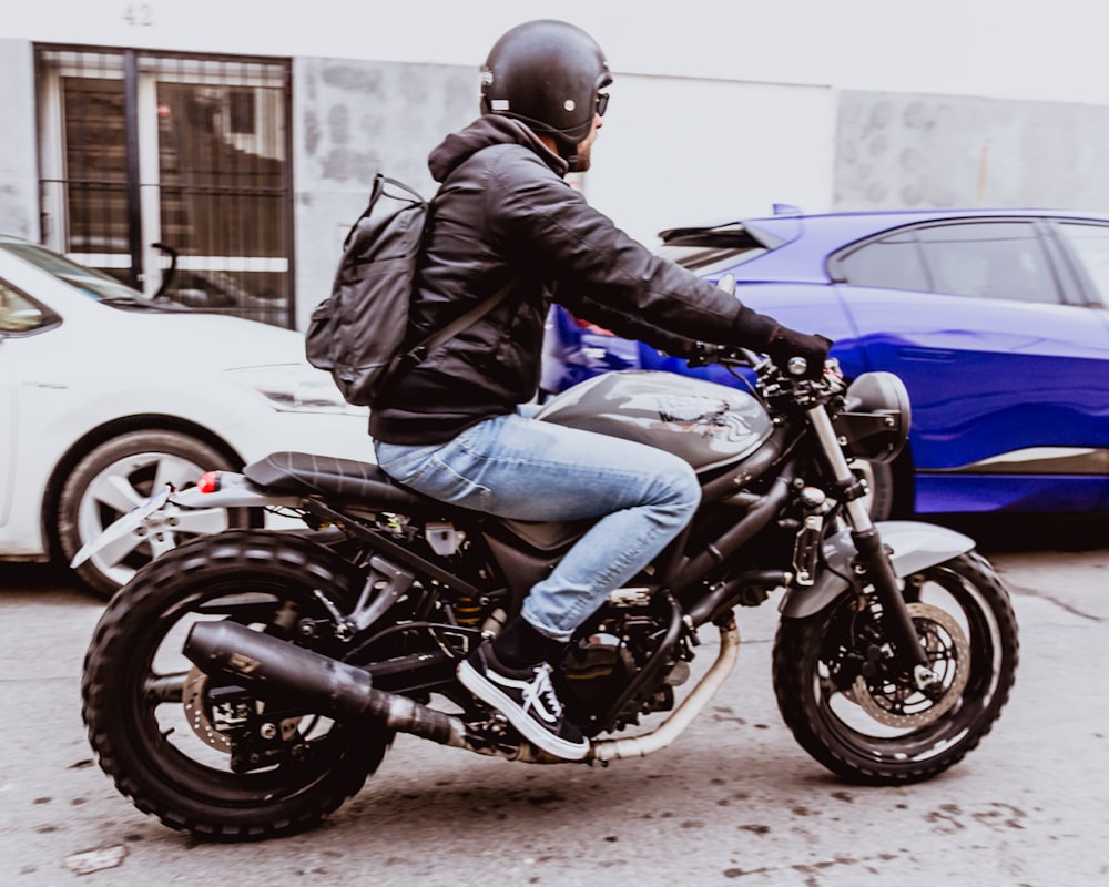 man in black leather jacket and blue denim jeans riding on black and blue sports bike