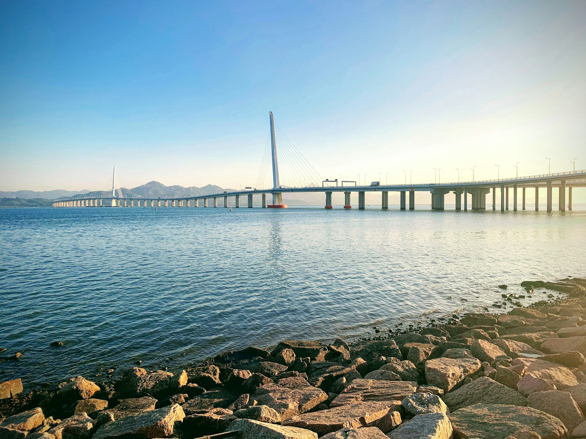 rocks on beach near bridge under blue sky during daytime