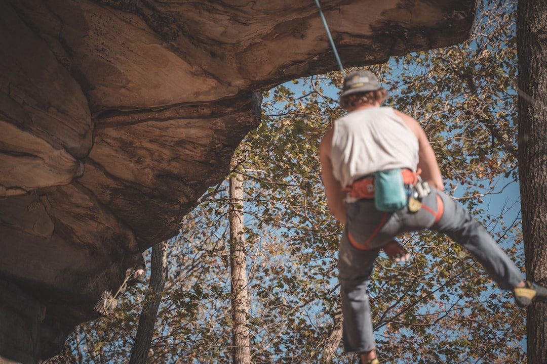 man in white tank top and blue denim jeans climbing on brown rock formation during daytime