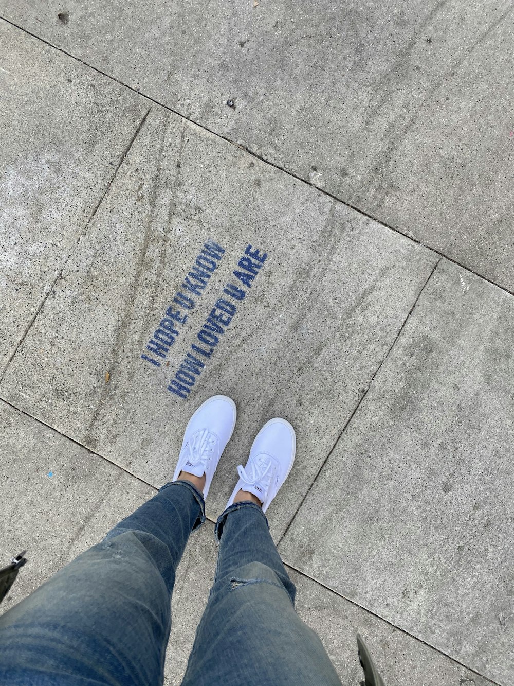 Persona in jeans blu denim e scarpe da ginnastica bianche in piedi sul pavimento di cemento grigio