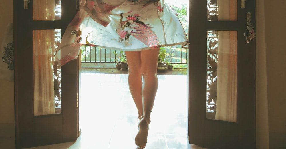 Mujer con vestido floral blanco y rosa de pie sobre baldosas blancas
