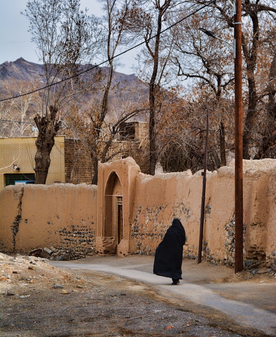 woman in black coat standing near brown concrete building during daytime in Natanz Iran