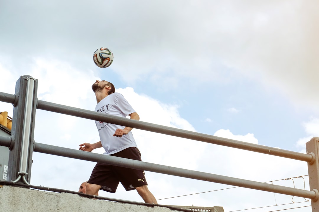 man in white t-shirt and black pants sitting on brown wooden fence during daytime