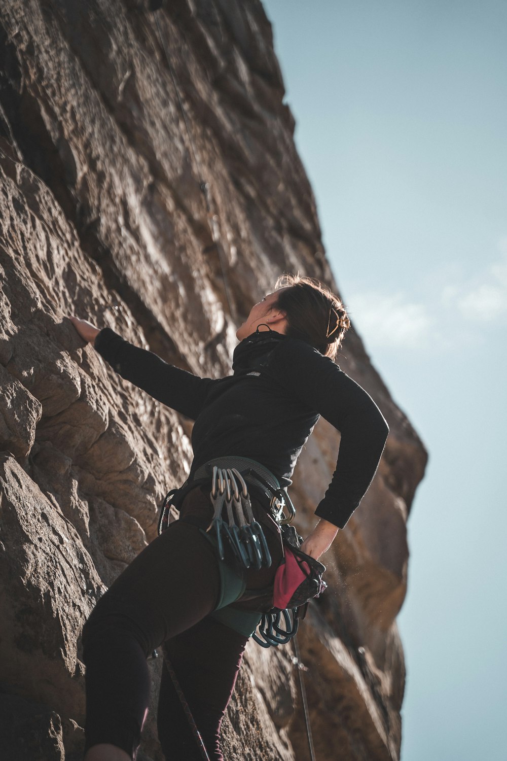黒の長袖シャツとブルーデニムのショートパンツを着た女性が、昼間に茶色の岩層を登っている
