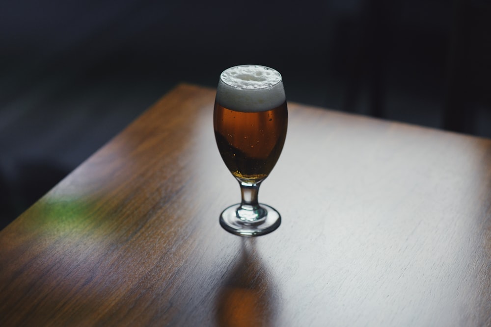 clear drinking glass with brown liquid on brown wooden table