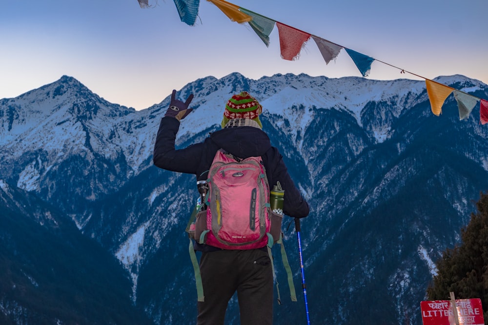 man in pink jacket and black pants with backpack standing on snow covered ground during daytime