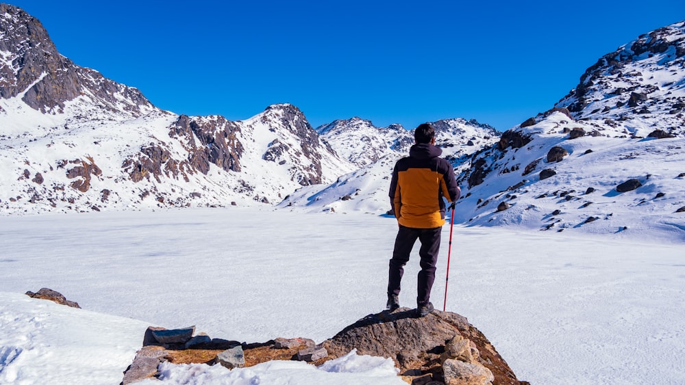 Hombre con chaqueta azul y pantalones negros de pie en el suelo cubierto de nieve durante el día