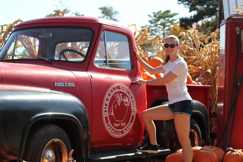 woman in white and brown dress leaning on red car during daytime