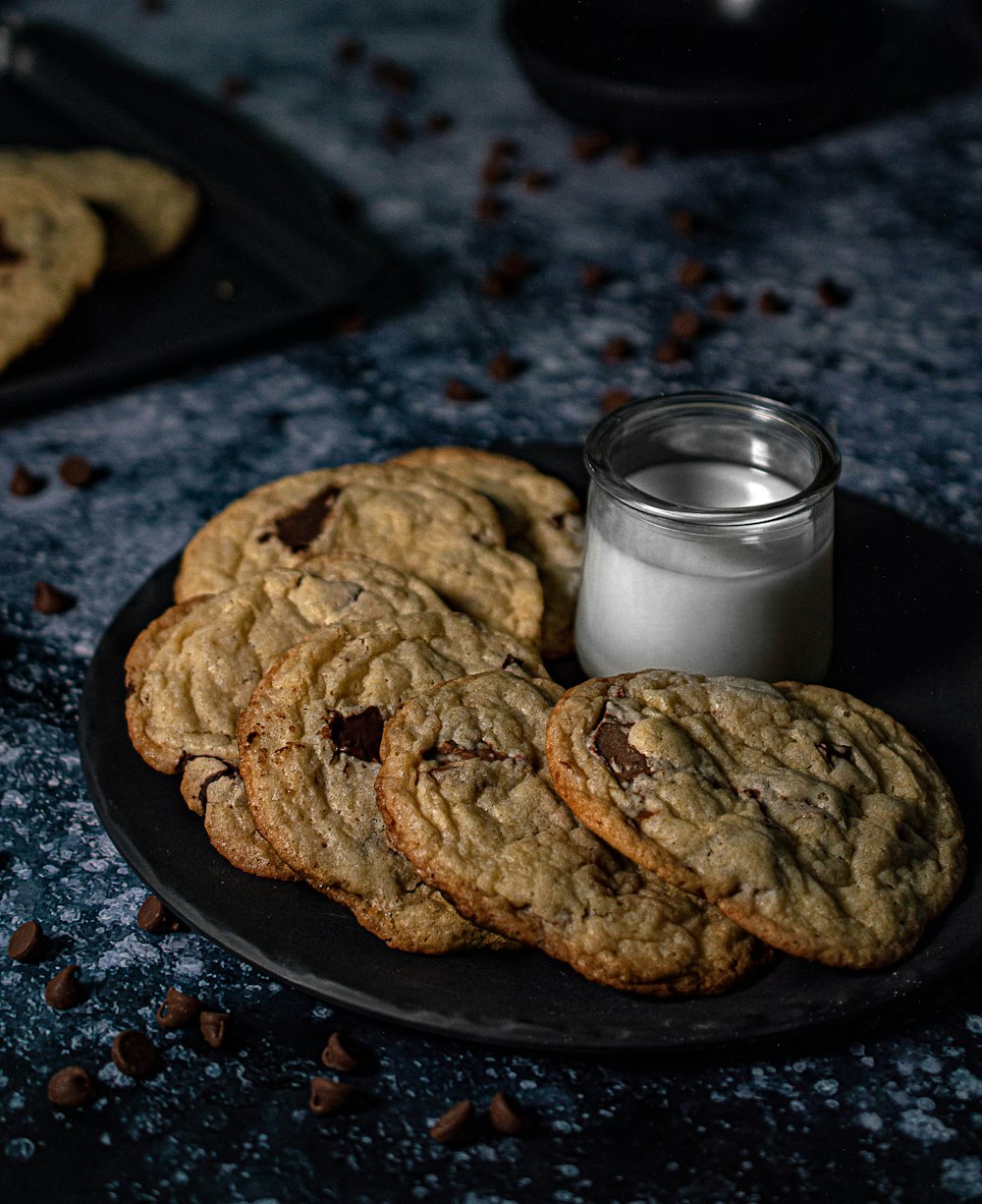cookies on black plate beside clear drinking glass with milk