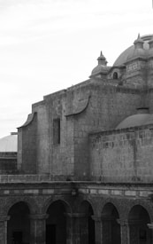A historic stone building with ornate arches and intricate carvings is visible, topped by a large dome and smaller towers. The architecture suggests an ancient or classical style.