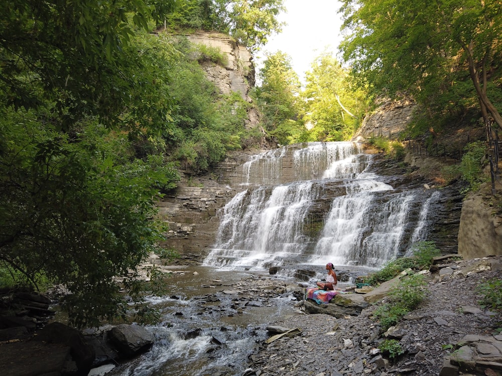 person in red jacket standing on rock near waterfalls during daytime