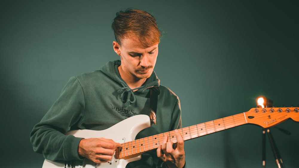 man in green button up shirt playing white electric guitar