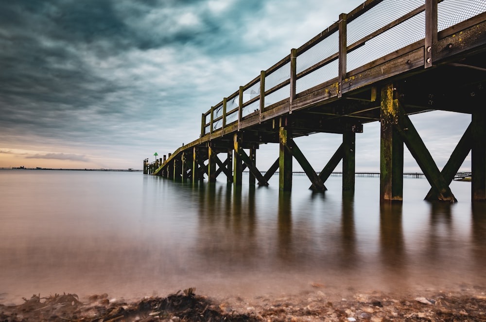 brown wooden dock on sea under cloudy sky during daytime