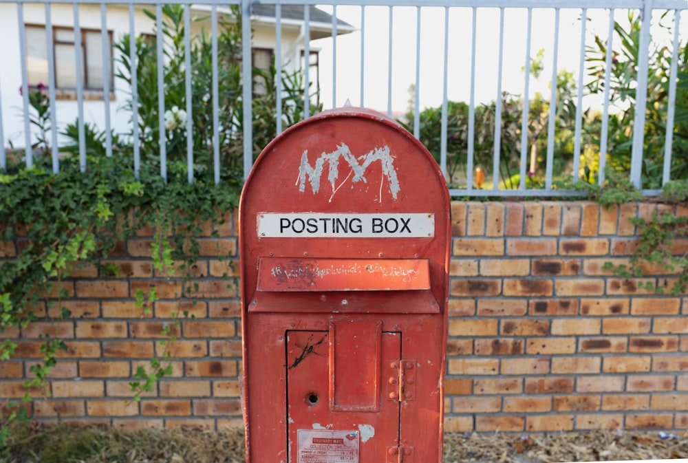 red mail box near brown brick wall