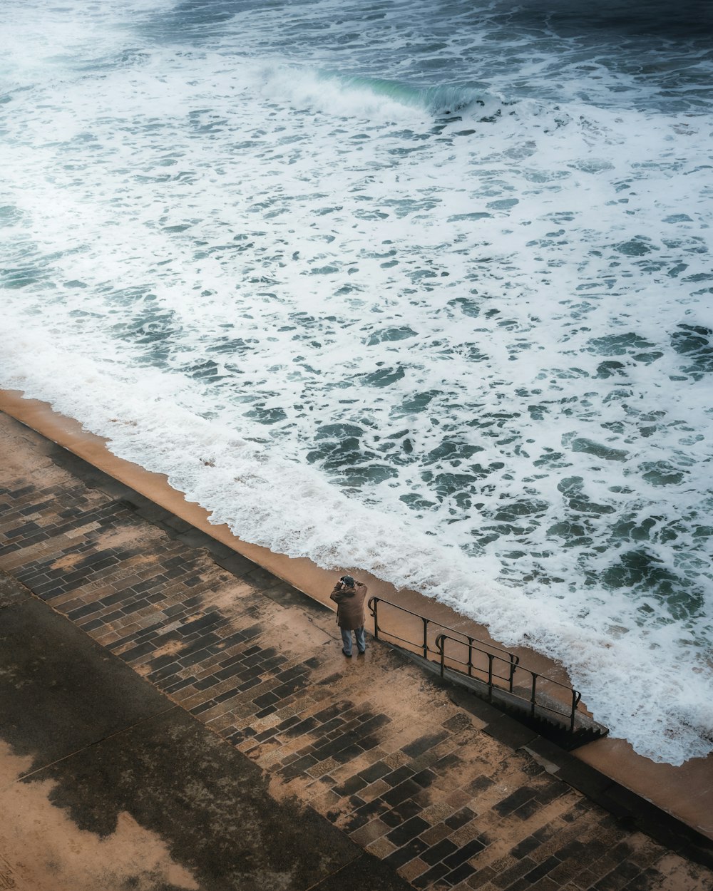 person standing on brown wooden dock near ocean waves during daytime