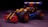 A colorful toy car built from interlocking plastic bricks, featuring large black wheels with red accents. The body of the car includes elements in yellow, red, black, and blue, and it is set against a dark, subtly textured background.