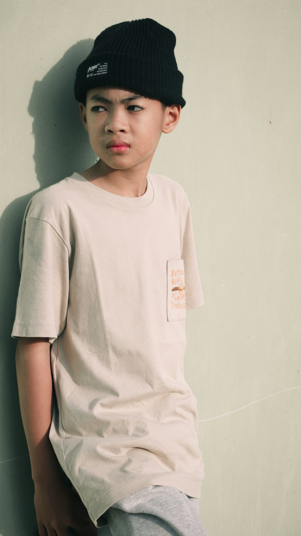 a young boy leaning against a wall wearing a hat