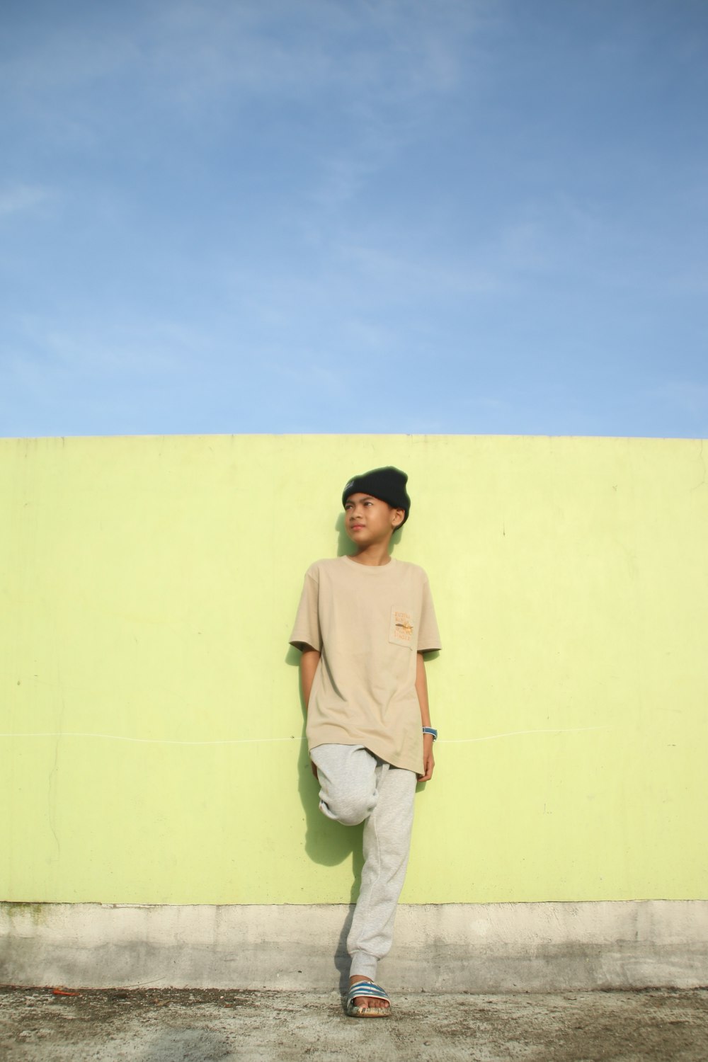 man in gray polo shirt and white pants standing beside yellow wall