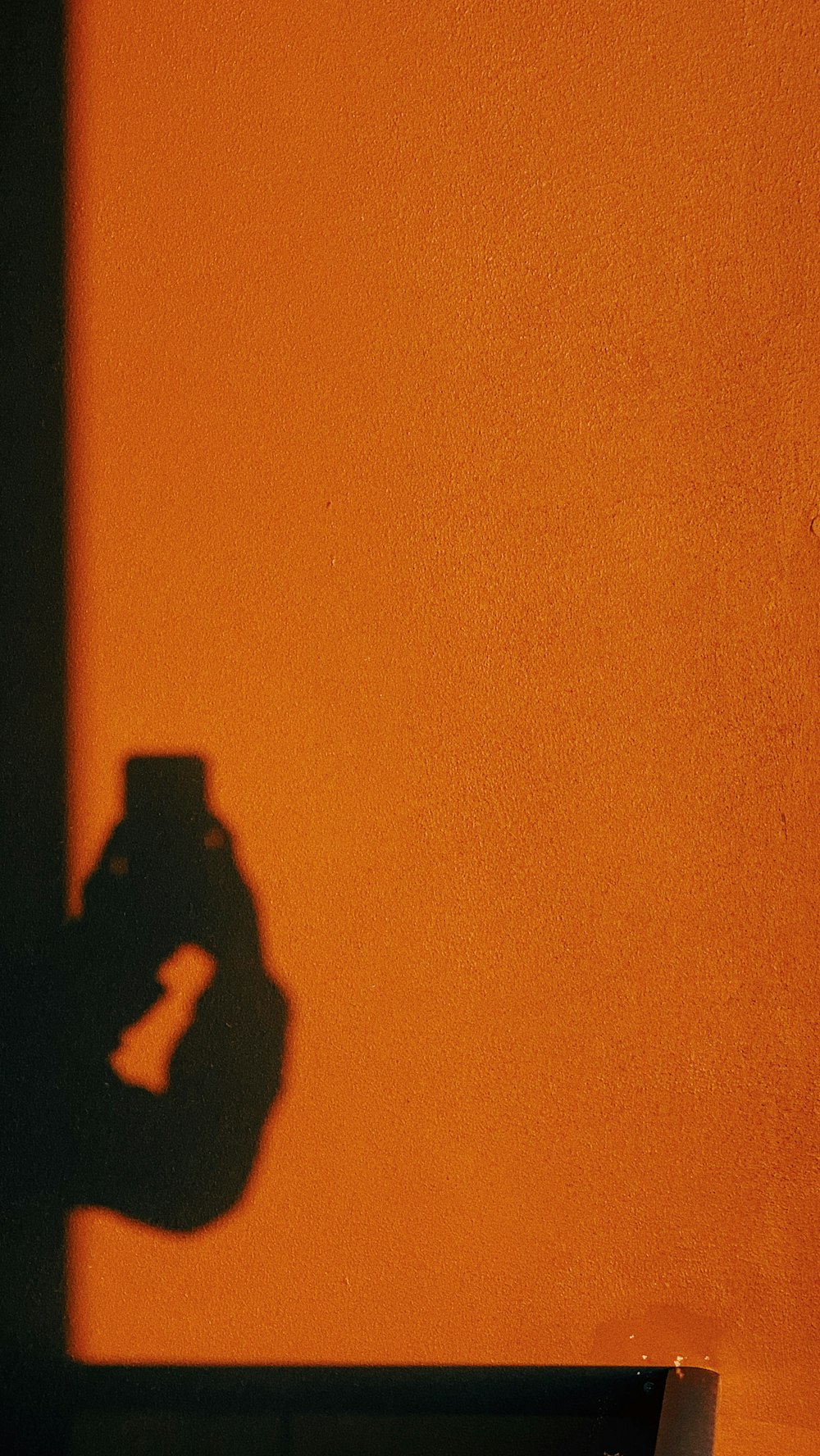 Person mit schwarzem Smartphone beim Fotografieren einer orangefarbenen Wand