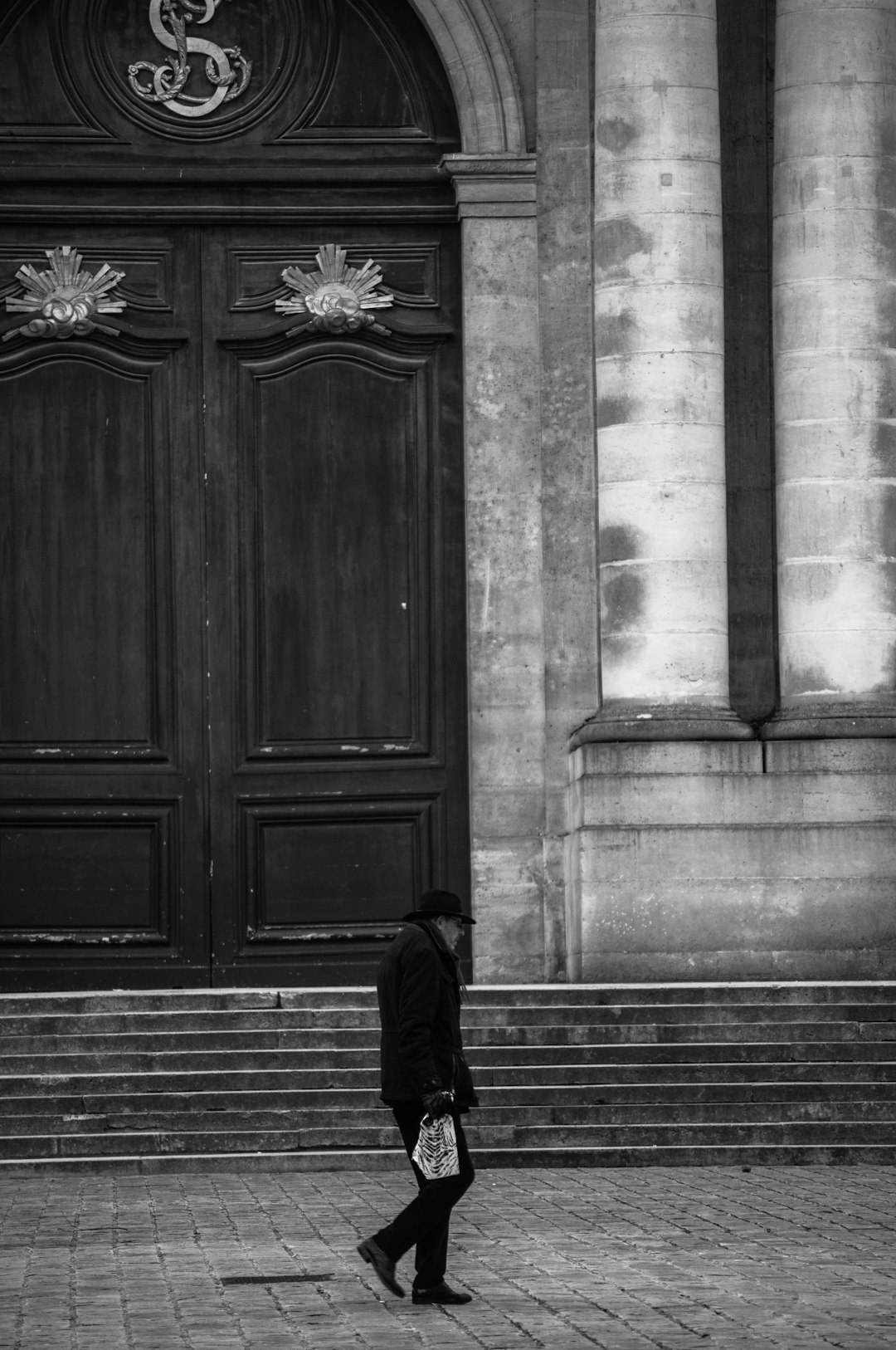 grayscale photo of man in black suit standing in front of wooden door