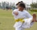 A smiling young boy in a white taekwondo uniform practicing a high kick on a bright training mat.