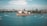 Aerial view of the Sydney Opera House situated on the waterfront, surrounded by several boats sailing in the harbor. The skyline of Sydney with numerous buildings forms the backdrop, under a partly cloudy sky.