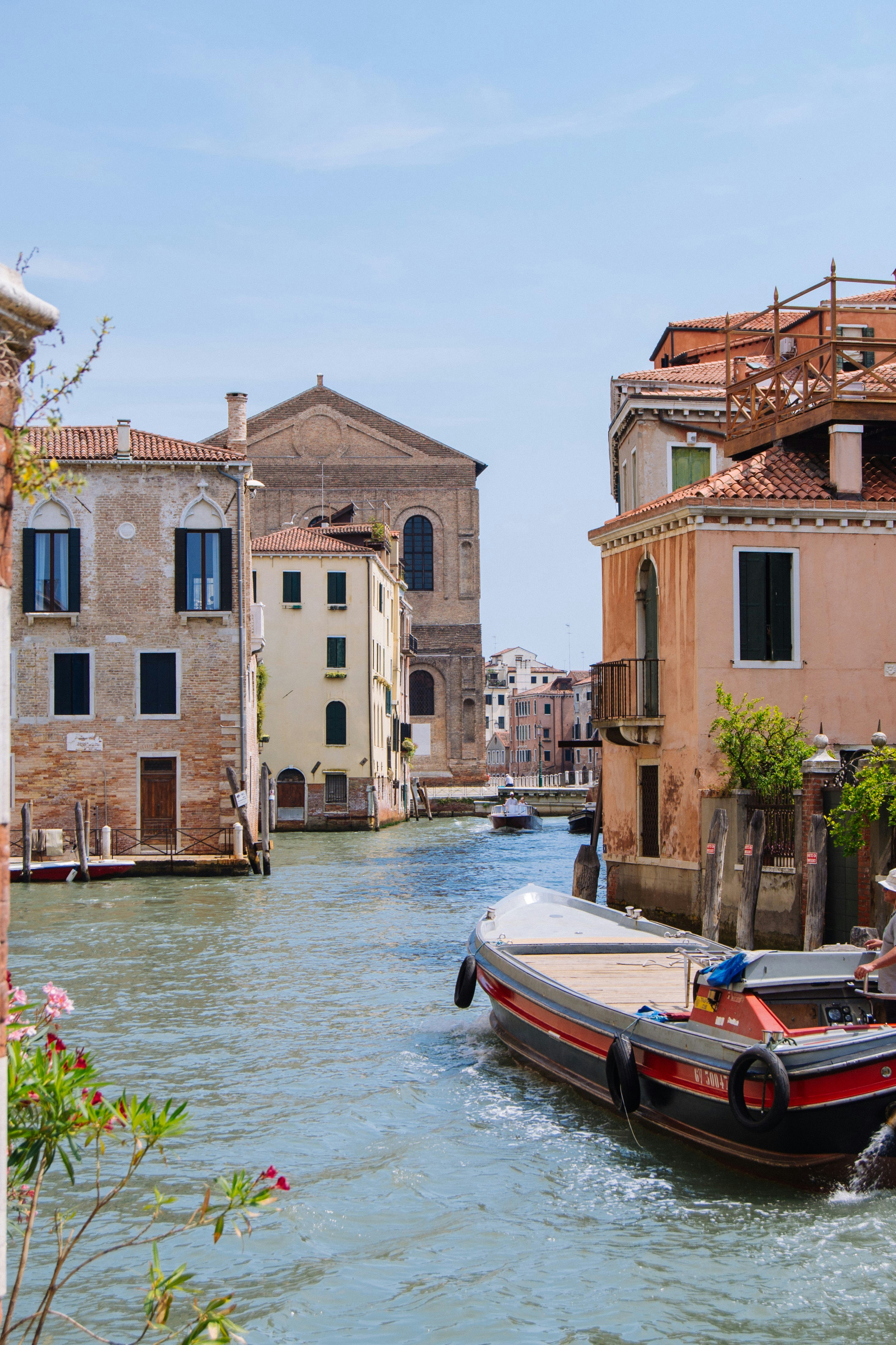 낮 동안 갈색 콘크리트 건물 근처의 물에 흰색과 빨간색 보트