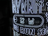 Bright neon signs with Korean and English text are displayed on a dark background. The design includes the words 'WE RUN SEO,' stylized in an illuminated outline font. The sign features a recognizable swoosh logo next to Korean characters encased in an elongated oval.