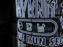 Bright neon signs with Korean and English text are displayed on a dark background. The design includes the words 'WE RUN SEO,' stylized in an illuminated outline font. The sign features a recognizable swoosh logo next to Korean characters encased in an elongated oval.