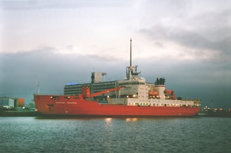 red and white cargo ship on sea under gray sky