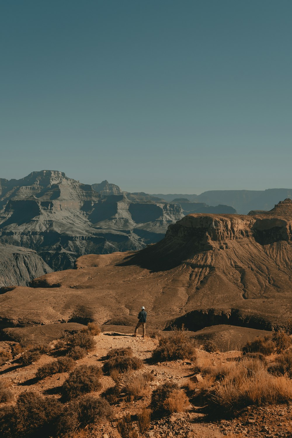 Persona che cammina sul campo marrone vicino alla montagna rocciosa marrone durante il giorno