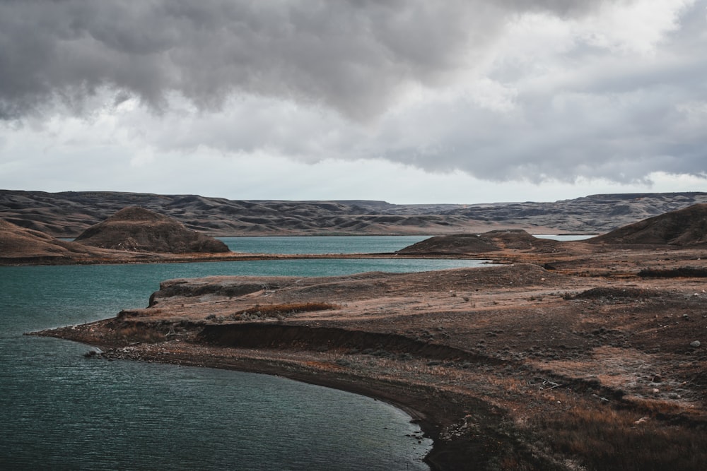 body of water near mountain under cloudy sky during daytime