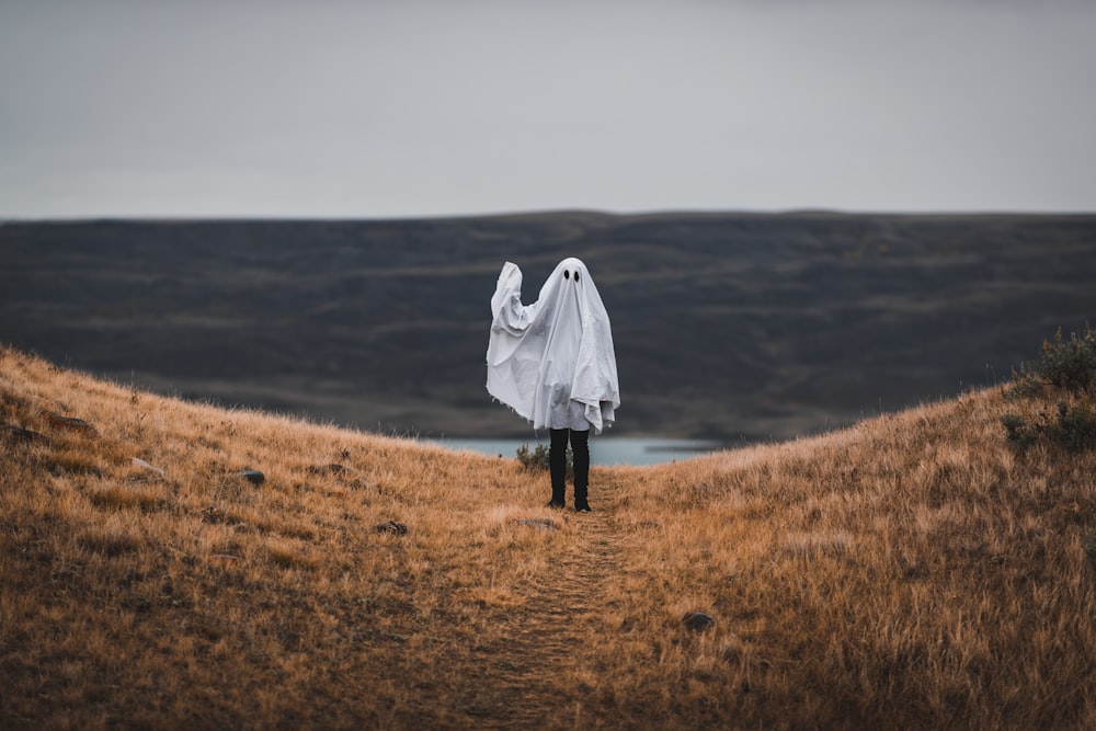 mulher no casaco branco em pé no campo marrom da grama durante o dia