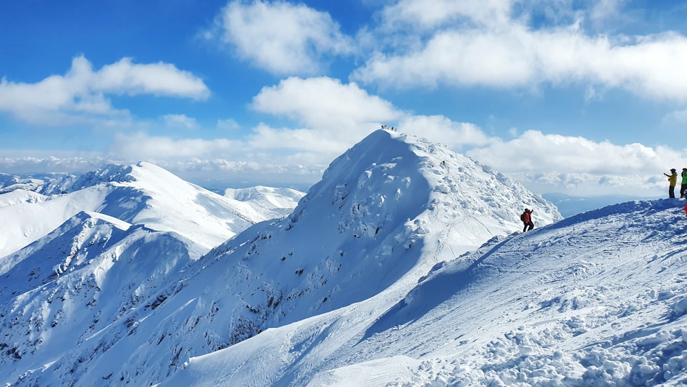 pessoa na jaqueta vermelha em pé na montanha coberta de neve sob o céu azul durante o dia