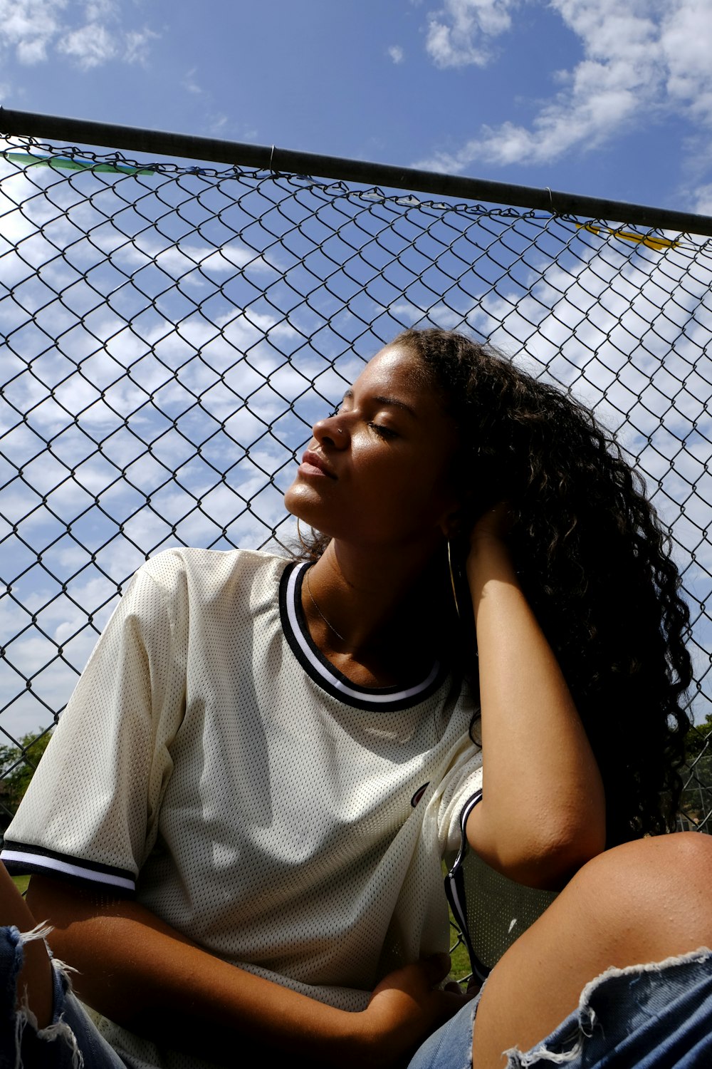 woman in white crew neck t-shirt leaning on chain link fence