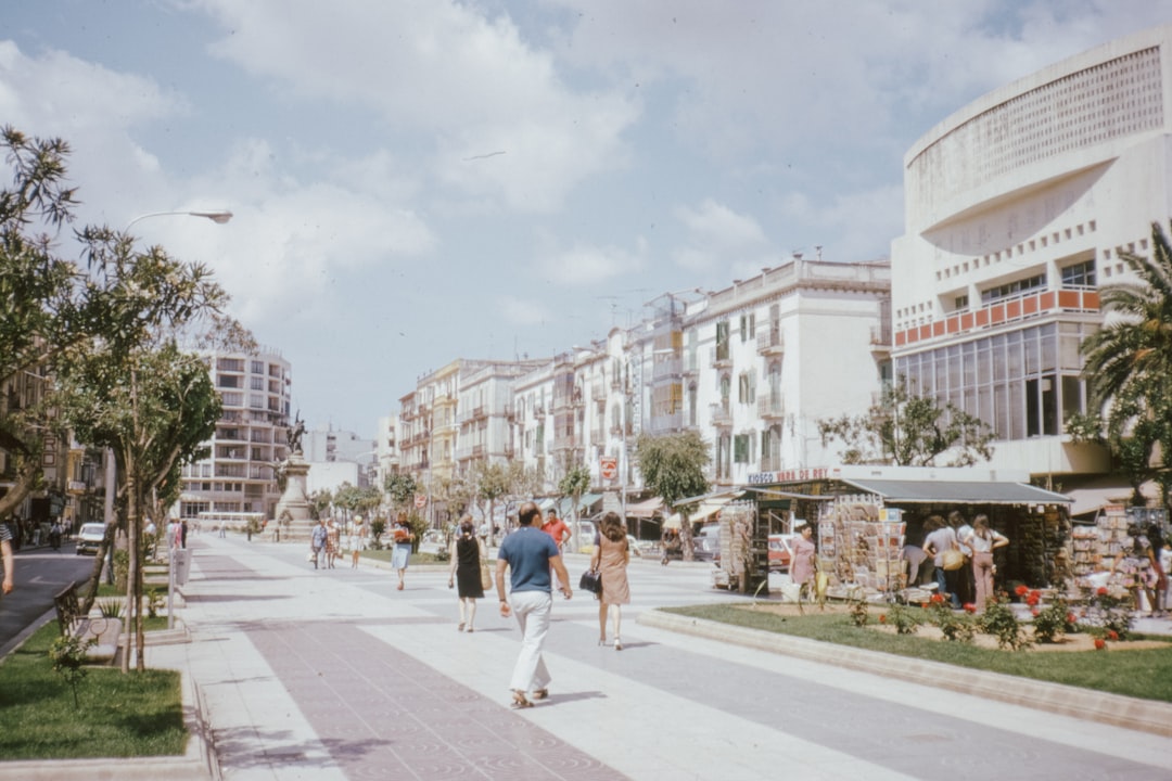 people walking on sidewalk near white concrete building during daytime