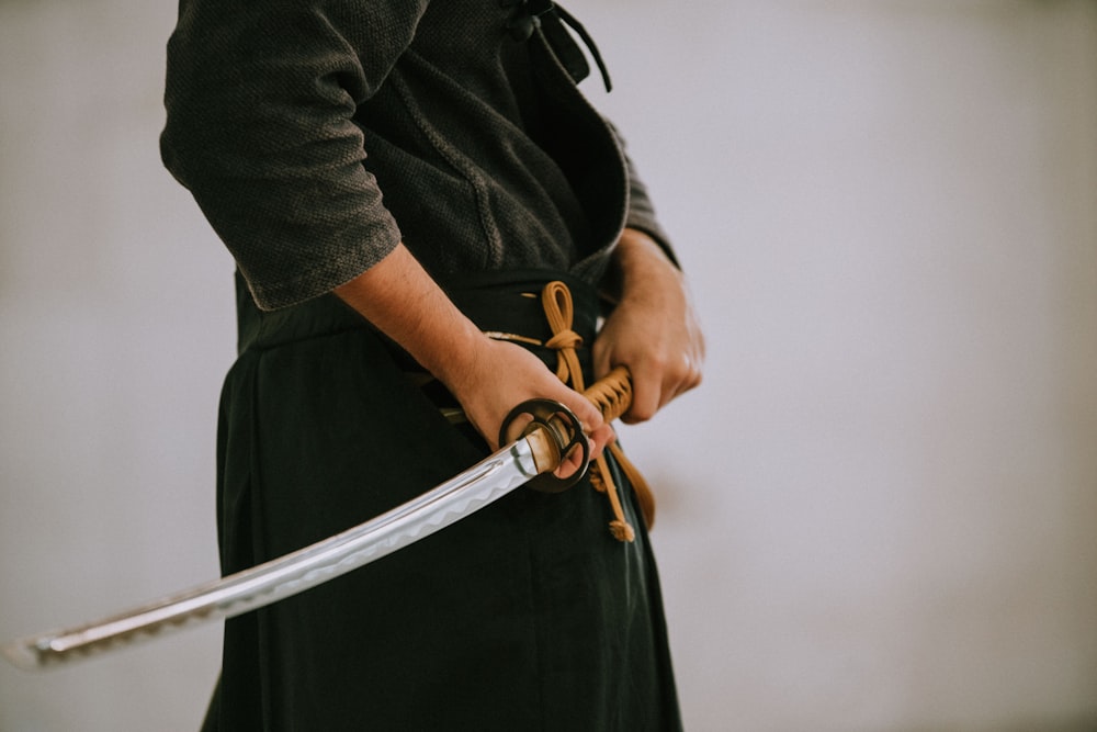 person in black long sleeve shirt and black skirt holding white leather belt